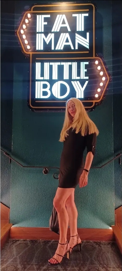 Rachael Fischer standing in front of the illuminated 'Fat Man Little Boy' neon sign.